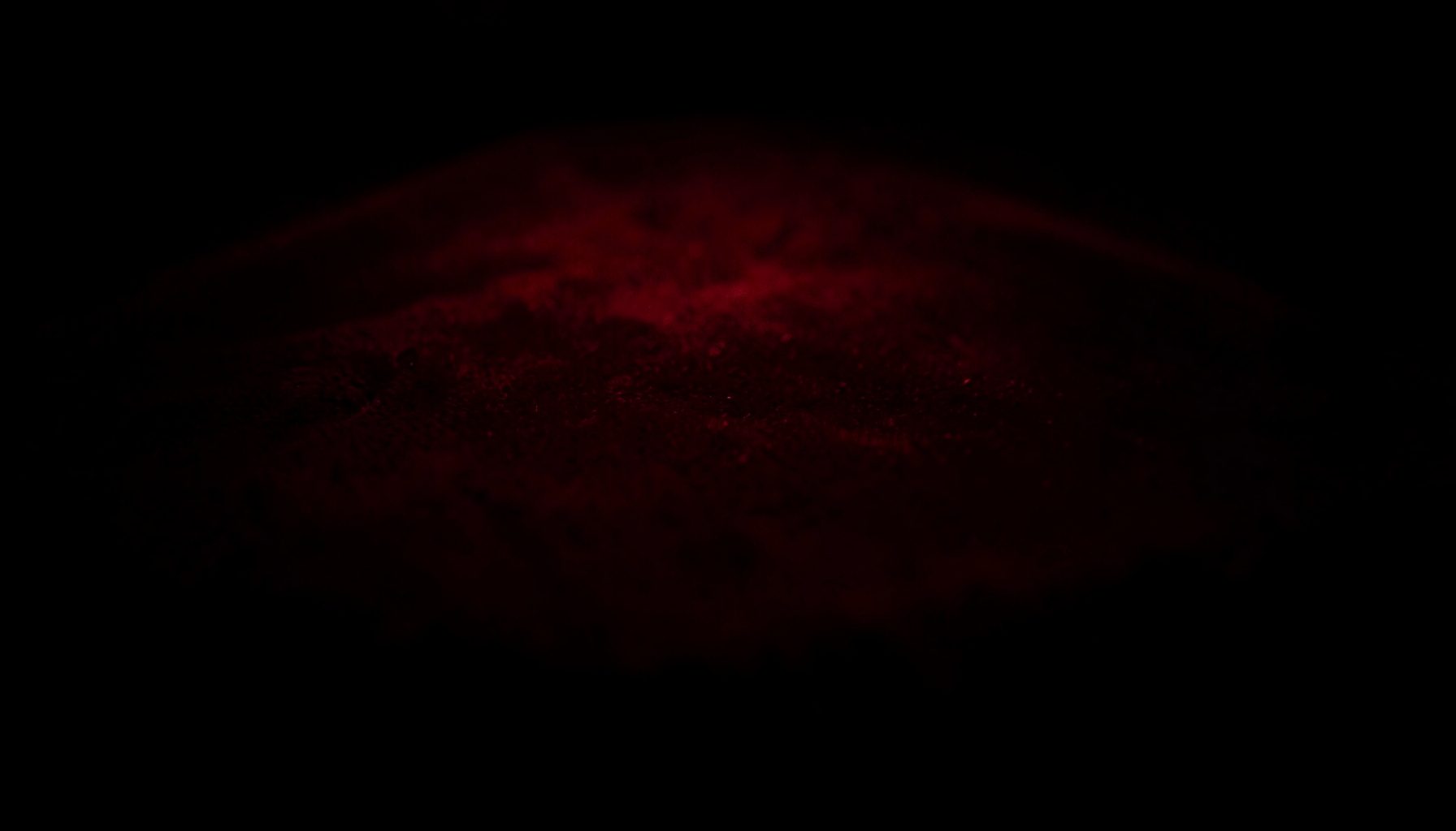 A dark, low-key photograph of a velvet table top in deep crimson and shadow, soft pool of light in the center