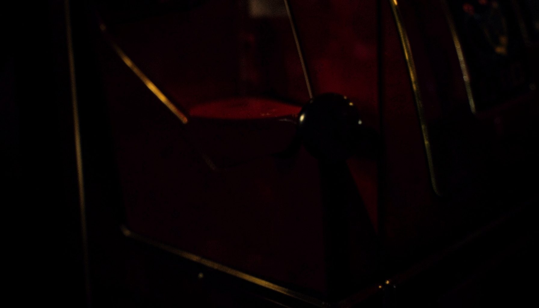 Close-up of a vintage slot machine lever in shadow, deep red panels, and faint gold trim catching warm light
