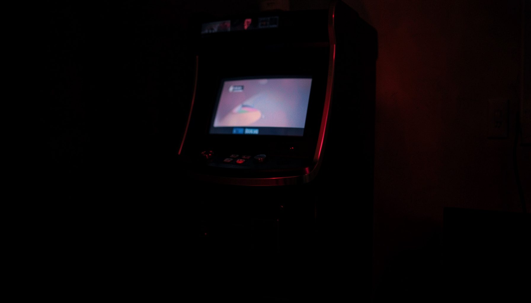 Dark slot machine cabinet with deep red accents and soft screen glow in a low-lit room