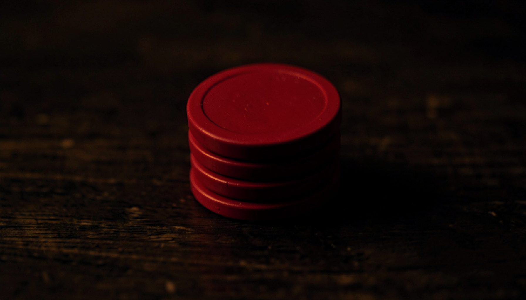 Stacked casino chips in deep red against a dark wood background, soft warm light