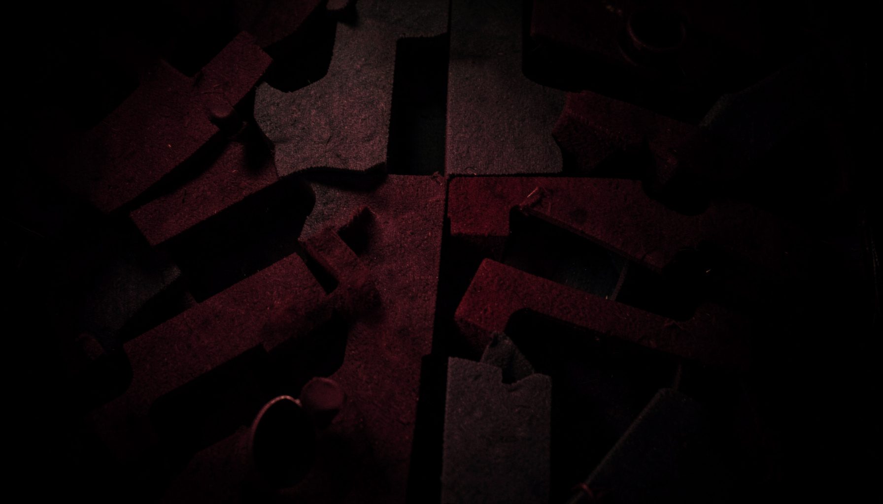 A dark overhead view of felt tables and slot banks in deep burgundy and charcoal, soft warm highlights, low-key atmospheric photograph