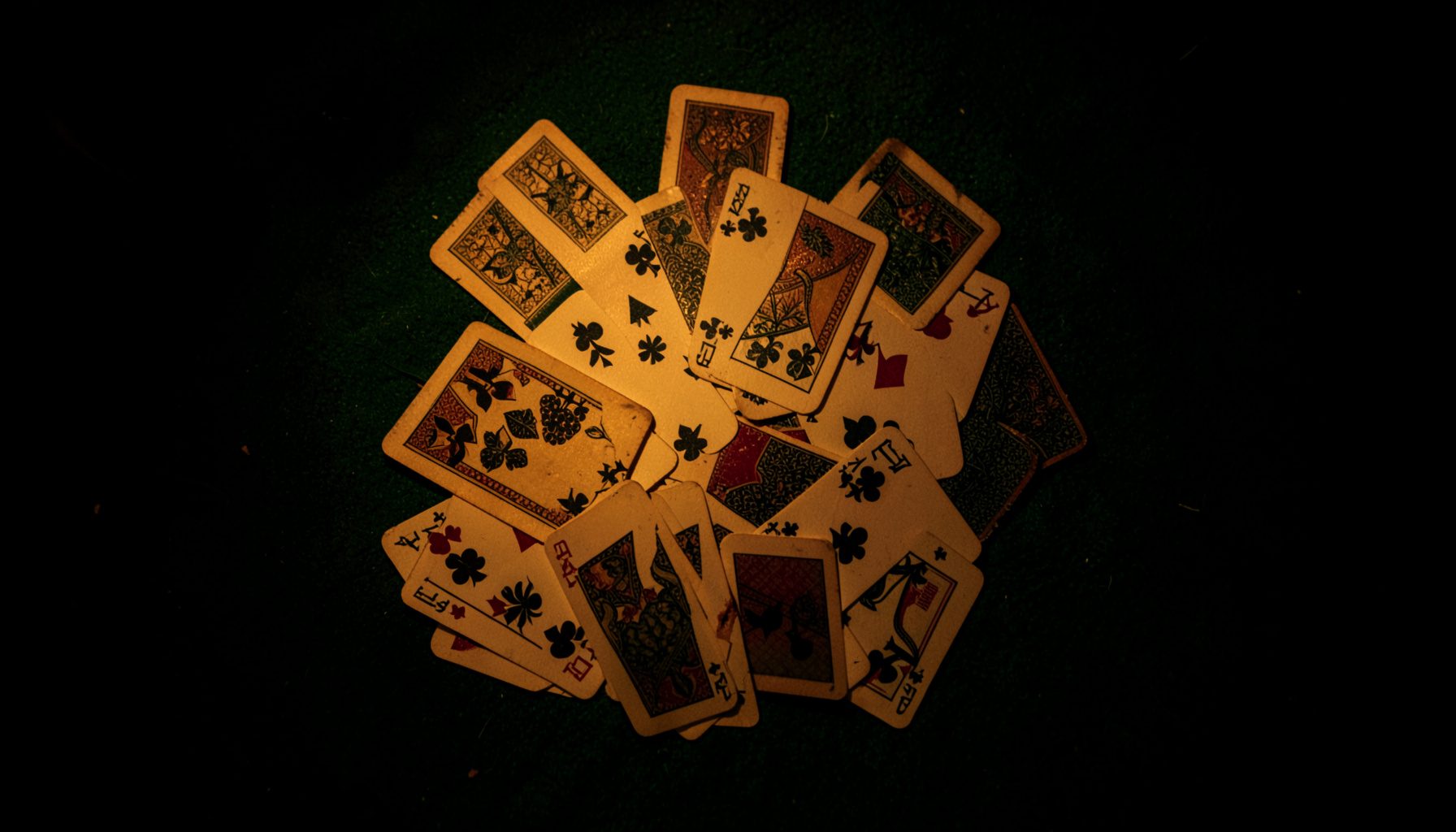 Overhead shot of playing cards spread on dark green felt with low amber lighting